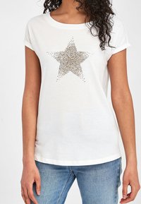 Hvid kortærmet T-shirt med et stort guld paliet-stjerne design foran. Blødt materiale og afslappet pasform, rullede ærmekanter.