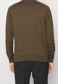 Brun stickad tröja med långa ärmar, rund hals och ribbade ärmmuddar och nedre kant. Slät textur, figurnära design och minimalistiska detaljer.