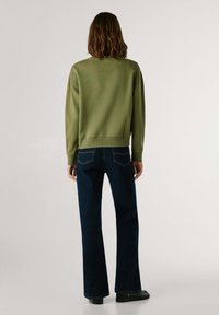 Felpa verde oliva con scollatura rotonda e polsini a costine abbinata a jeans svasati blu scuro con cuciture a contrasto e vita alta.
