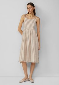 Gestreiftes Midi-Kleid in Beige und Creme, mit Spaghettiträgern und gerafftem Bund. Leichter Stoff mit glatter Textur, kombiniert mit flachen Schuhen.