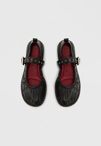 Čierne kožené topánky so zaoblenou špičkou, našuchorenou textúrou a bočným remienkom so striebornou prackou. Červené vložky a ozdobné cvoky okolo okrajov.