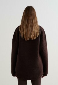 Bruine, oversized fleece pullover met een textuurafwerking, lange mouwen en een afgeronde zoom. De achterkant toont het zachte, gezellige materiaal.