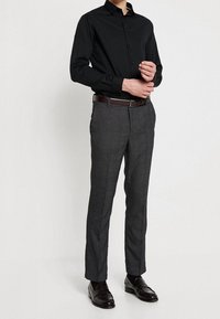 Zwarte overhemden met kraag, grijze gemusterde broek en donkerbruine leren schoenen. De broek heeft een getailleerde snit en een riem.