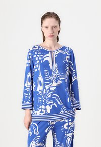 Blauwe en witte tuniek met een gedurfde abstracte print, lange mouwen en een ronde hals met een centrale knoopdetail.