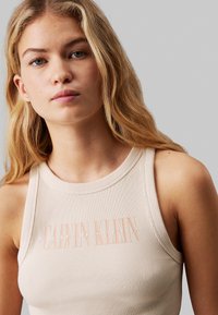 Top in cotone beige a coste con collo alto e audaci scritte bianche e rosa, che riportano il nome del marchio e "Nineteen Seventy Eight."