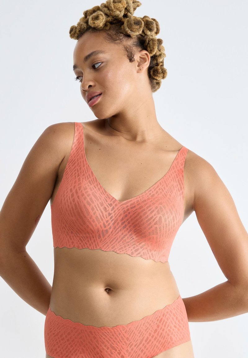 Bralette inalámbrico de color durazno con escote en V, bordes ondulados y un patrón geométrico texturizado, hecho de un material elástico suave.
