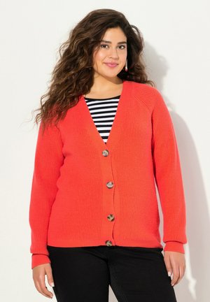 Cardigan lavorato a maglia di colore rosso corallo con scollatura a V, apertura con bottoni e texture a coste. Maniche lunghe e vestibilità comoda, abbinato a una maglietta a righe bianco e nero.