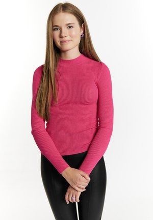 Säärenysä kimaltavassa vaaleanpunaisessa ribbimateriaalissa, korkeakauluksinen muotoilu. Yhdistetty mustiin leggings-housuihin, varustettuna kerrosrenkaalla.