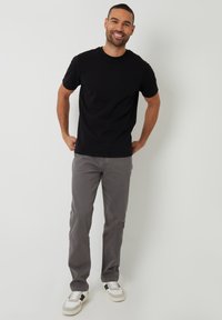 Camiseta negra de manga corta con un corte clásico, combinada con pantalones gris de corte slim y zapatillas blancas con acentos en negro.