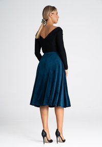 Czarny top z długim rękawem i turkusowa spódnica w kształcie litery A o gładkiej fakturze, zestawione z czarnymi szpilkami, widok z tyłu.