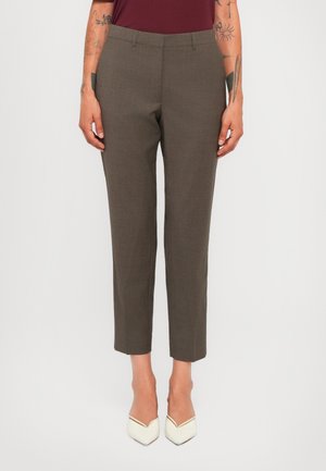 Pantalons raccourcis marron à coupe droite portés avec des talons aiguilles blancs, bras tatoués visibles et un haut bordeaux.