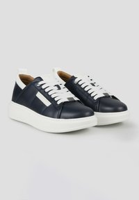 Marine leren sneakers met witte veters en een dikke witte rubberen zool. Heeft minimale stiksels en een klein metalen accent aan de zijkant.