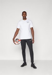 Hvid kortærmet t-shirt med "PARIS" tekst, parret med sort slim-fit bukser med et Nike-logo, holder en mønstret fodbold.