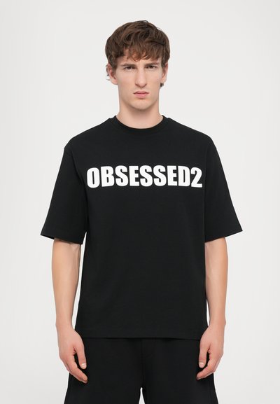 Schwarzes Baumwoll-T-Shirt mit kurzen Ärmeln und Rundhalsausschnitt. Die Vorderseite zeigt fettgedruckten, weißen Text mit der Aufschrift "OBSESSED2."