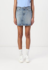 Light blue denim skirt with a fitted design, frayed hem, and classic five-pocket styling, paired with white sneakers and socks.