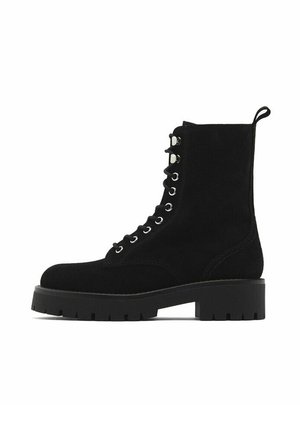 Bottines en daim noir avec un laçage à l'avant, des œillets argentés et une semelle en caoutchouc épaisse. Dotées d'une bride à l'arrière pour faciliter l'enfilage.
