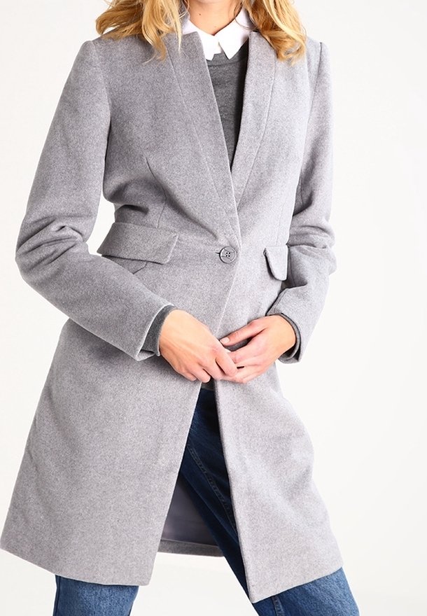 Abrigo gris de mezcla de lana con silueta entallada, cuello con muesca, cierre de un solo botón y bolsillos laterales, llevado sobre un suéter gris y jeans.