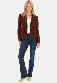 Bordowa marynarka z falbanami i sześcioma guzikami, zestawiona z ciemnoniebieskimi dżinsami i beżowymi szpilkami. Gładki materiał, zrównoważony fason.