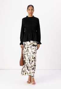Black smocked long-sleeve top paired with a flowing cream skirt featuring a black and brown abstract pattern; includes a brown handbag.