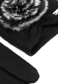 Cappello di lana nera con un pom-pom in faux fur bianco e nero sulla parte superiore, abbinato a guanti di lana neri, entrambi caratterizzati da una texture morbida.