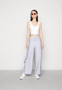 Top cropped branco com detalhes de botões, combinado com calças largas florais em lavanda, ténis brancos e uma mala lavanda.