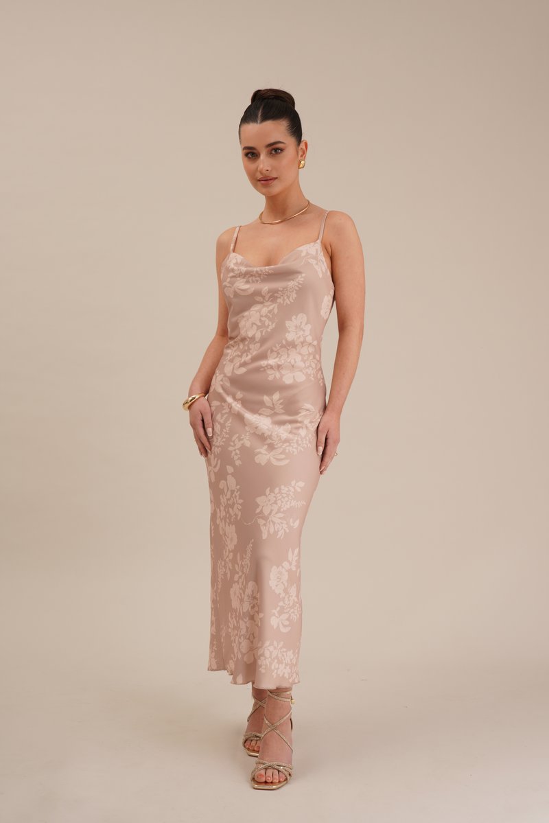 Vestido de cetim com padrão floral, na cor rosa claro, com alças finas, silhueta ajustada e comprimento até meio da panturrilha, combinado com sapatos de salto com tiras.