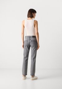 Grå denim jeans med rette ben, baklommer og en svart etikett på midjebåndet, satt sammen med en hvit tanktop og sneakers.