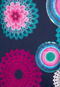 Kolorowe okrągłe wzory z tkaniny na ciemnoniebieskim tle, w tym różowo-zielony wzór kwiatowy, motyw przypominający szydełkowanie w kolorze magenty oraz koncentryczne okręgi w odcieniach niebieskiego i różowego.