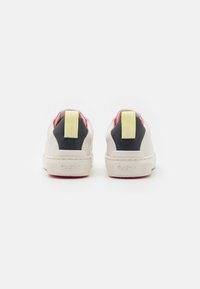 Sneakers med en overdel i hvid læder, sorte hæl-accenter, lyserød foring og en gul mærket hælflap; struktureret gummisål med logodetalje.
