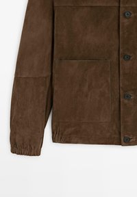 Brauner Wildlederjackenärmel und Vorderseite mit großer Tasche, elastischem Bündchen und dunklen Knöpfen vor weißem Hintergrund.