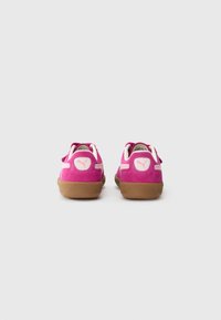 Un paio di sneakers in suede rosa con i loghi bianchi Puma su suole in gomma beige, viste da dietro su uno sfondo bianco semplice.