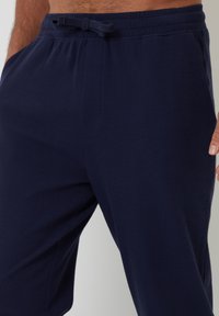Námořnické modré vzorované pyžamové kalhoty s elastickým pasem, vnitřní šňůrkou a bočními kapsami. Materiál vypadá měkký a lehký.