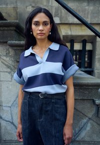 Tricou polo cu dungi bleumarin și albastru deschis, cu guler, combinat cu pantaloni din denim închis cu talie înaltă și o curea neagră cu cataramă argintie.