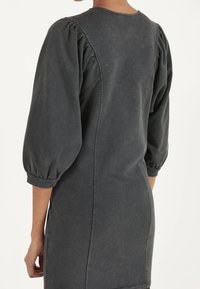 Vestido gris carbón con mangas abullonadas, cuello redondo y costuras visibles. Confeccionado en un tejido suave y texturizado, de diseño hasta los tobillos.
