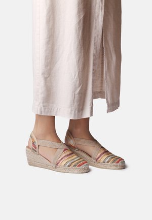 Pies con alpargatas beige de cuña con tejido multicolor tejido y tiras elásticas en el tobillo, combinadas con pantalones de lino claros.