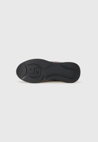 La semelle de la chaussure présente un matériau en caoutchouc noir avec une surface texturée et un design courbé. Un logo notable et des motifs de traction sont inclus.