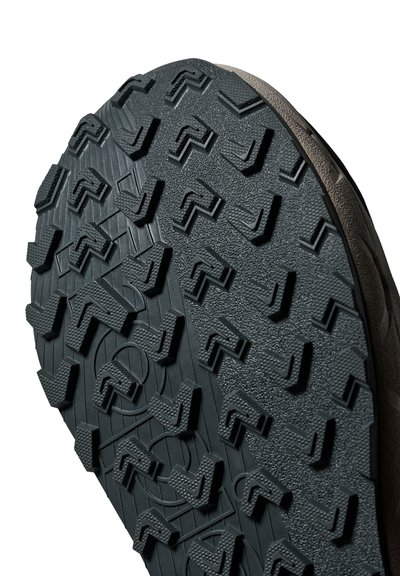 Gros plan sur le motif de la semelle d'une chaussure de randonnée en caoutchouc noir, avec des crampons profonds et angulaires pour une meilleure adhérence et traction.