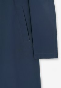 Granatowy płaszcz o gładkiej teksturze, skośnej kieszeni oraz ustrukturyzowanych rękawach z wyraźnymi detalami przeszycia.