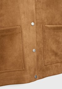 Brun ruskindsjakke med sølvfarvede trykknapper, to forlommer og en blød tekstur. Det overordnede design er minimalistisk og funktionelt.