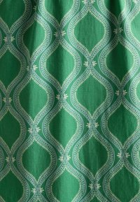 Grüner Stoff mit einem sich wiederholenden Muster aus länglichen Rhombusformen, die in Hellblau umrandet sind, mit weißen Motiven, die eine glatte Textur zeigen.