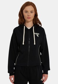 Felpa con cappuccio nera con zip, coulisse color crema, logo e piping bianco a contrasto, realizzata in tessuto morbido, abbinata a pantaloni della tuta neri.