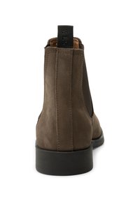 Brown suede Chelsea boots featuring a pull tab, elastic side panels, and a black rubber sole; smooth texture with stitched detailing.