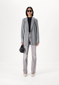 Gray houndstooth blazer with a relaxed fit, paired with gray jeans. Black top, small black handbag, and pointed beige heels complete the outfit.