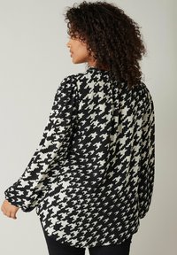 Sort-hvid houndstooth mønster bluse med lange ærmer, høj hals og en let løs pasform, med en struktureret stof.