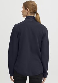 Dark navy fleece pullover with a high collar, long sleeves, and a textured surface. Features a curved hem and minimalistic design.