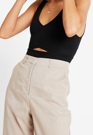 Czarny top bez rękawów z głębokim dekoltem w kształcie litery V i detalem w postaci wycięcia, połączony z beżowymi spodniami o wysokim stanie z kieszeniami z przodu i gładką fakturą.