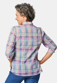 Camicetta a quadri multicolore con maniche corte arrotolate, colletto e spacchi laterali. Realizzata in tessuto leggero con una superficie liscia.