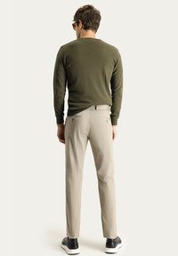 Suéter de manga larga verde oliva, pantalones beige claros y zapatillas negras con suelas blancas, vistos desde la parte de atrás, mostrando un ajuste casual.