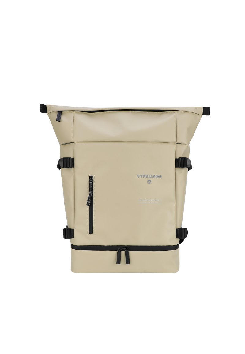 Beige batoh na rolovací uzávěr vyrobený z odolného materiálu s černými kovovými prvky, obsahující přední zipovou kapsu a nastavitelné boční popruhy.