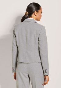 Grau taillierter Blazer aus strukturiertem Stoff, mit figurbetontem Schnitt, Reverskragen und Dreiknopfdetails an den Ärmeln.
